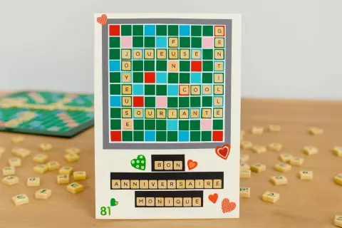 Carte d'anniversaire personnalisée avec un plateau de Scrabble relooké formant "Joyeuse" et "Anniversaire Monique".