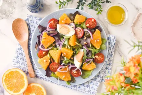 Ensalada de naranja vibrante con tomates cherry, huevo duro, cebolla morada y piñones. Una delicia fresca y colorida.