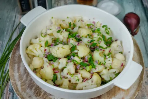 Frischer blumenkohl salat mit roten Zwiebeln und Schnittlauch, serviert in einer weißen Schüssel auf rustikalem Holz.