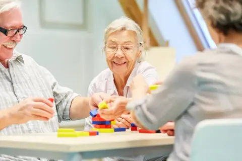 Senioren bauen mit bunten Klötzen. Ein Lächeln auf den Lippen zeigt, wie wichtig solche Aktivitäten für die demenz behandlung sind.