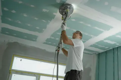 Hombre lijando techo de yeso, preparándolo para el aislante.