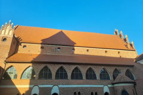 Olsztyn zamek, ceglana budowla z pomarańczowym dachem i łukowymi oknami, w blasku słońca.