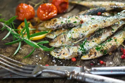 Délicieuses sardines à la plancha, parsemées d'herbes fraîches, accompagnées de tomates cerises rôties et d'une branche de romarin sur fond de bois rustique.