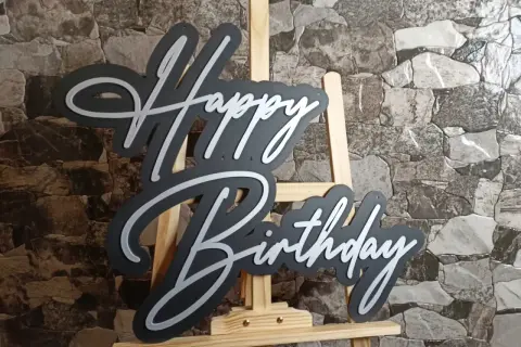 Czarny napis "Happy Birthday" z białymi obrysami, stojący na sztaludze. Idealny na życzenia "sto lat"!