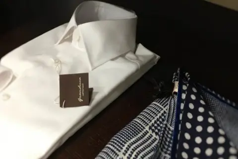 Camicia bianca da uomo con abbottonatura maschile impeccabile, accanto a un fazzoletto da taschino a pois e a quadretti.