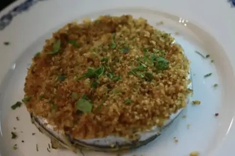 Tortino di alici dorato e croccante, guarnito con prezzemolo fresco, servito su un piatto bianco con bordo blu.