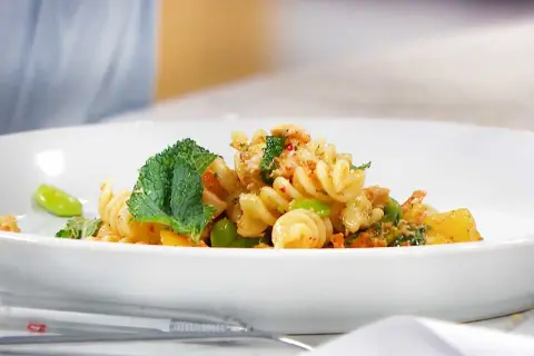 En läcker pastasallad med kyckling, gröna bönor och mynta på en vit tallrik.