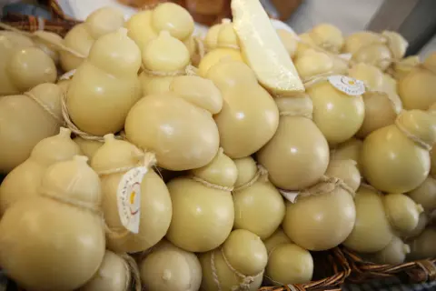 Un cesto pieno di formaggio podolico, alcuni a forma di pera, legati con spago. Un pezzo di formaggio è appoggiato sopra.