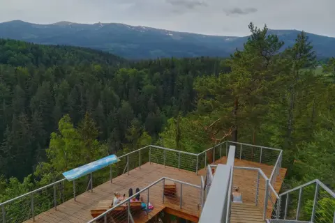 Drewniany punkt widokowy w Karpaczu z widokiem na góry i las. Dwie osoby odpoczywają na platformie.