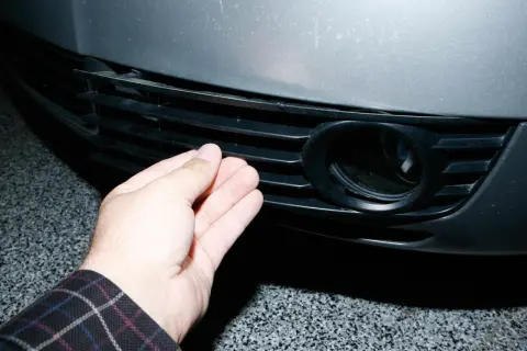 Dłoń naciska na kratkę zderzaka Audi A6 C5, obok otworu na światło przeciwmgielne.
