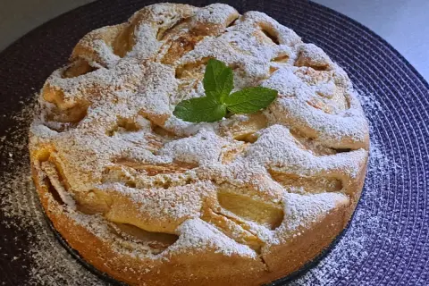 Szybkie tanie ciasto z jabłkami, posypane cukrem pudrem i ozdobione listkiem mięty. Idealne na deser.