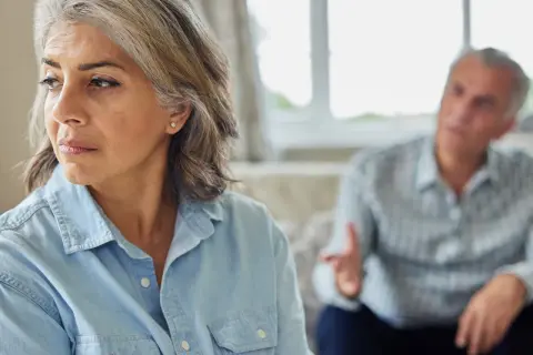 Een vrouw kijkt weg tijdens een gesprek, de man op de achtergrond gebaart. Dit beeld roept de vraag op: wanneer heeft relatietherapie geen zin?