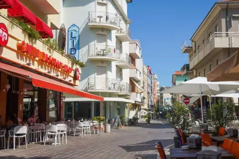 Passeggiata serale a Gabicce Mare: tavolini all'aperto di un caffè, hotel Lido e negozi colorati.