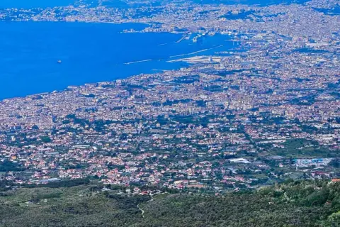 Blick über die weitläufige Stadt Neapel, Italien, mit dem blauen Meer und dem Hafen im Hintergrund.