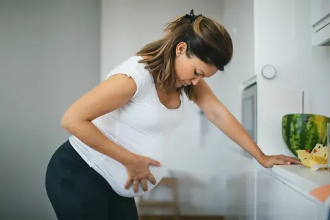 Schwangere Frau mit Hand auf dem Bauch, die sich vorbeugt. Sie fragt sich, ab wann Vorwehen auftreten können.