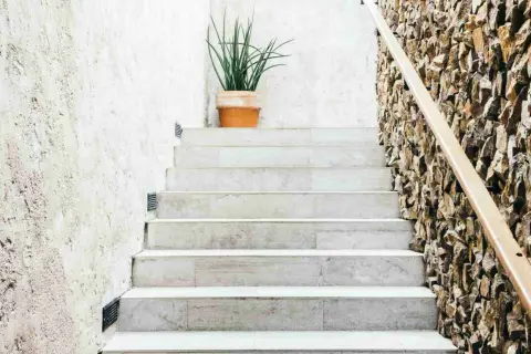 Escalier en marbre avec une plante en pot sur la première marche. Le carrelage de l'escalier, marche ou contremarche, est mis en valeur par un mur de pierres naturelles.