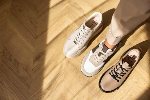 Ciekawe, jakie buty do cygaretek zimą? Na drewnianej podłodze leżą beżowe sneakersy i eleganckie botki.