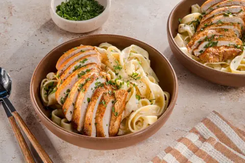Zwei Schüsseln cremiger Pasta mit geschnittenem Hähnchenbrustfilet, bestreut mit Petersilie. Ein köstliches Chicken Alfredo Rezept für jeden Anlass.