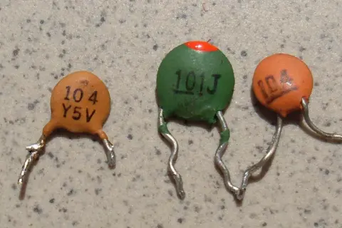 Trzy ceramiczne kondensatory z widocznymi oznaczeniami, np. "104".