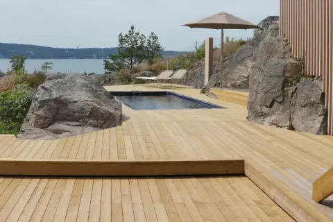 En stor altan i trä med pool och solstolar, omgiven av klippor och med utsikt över havet. Trall mått är perfekt för detta sommarparadis.