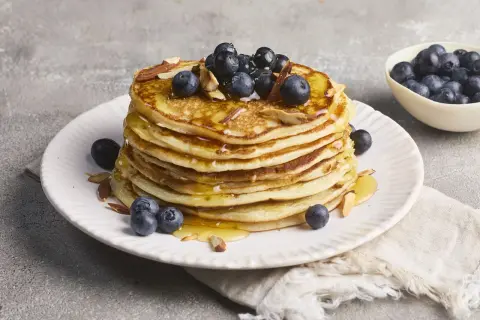 Stapel goldbrauner Pancakes, garniert mit Blaubeeren, Mandelsplittern und Honig. Ein köstliches Rezept für High Protein Pancakes.
