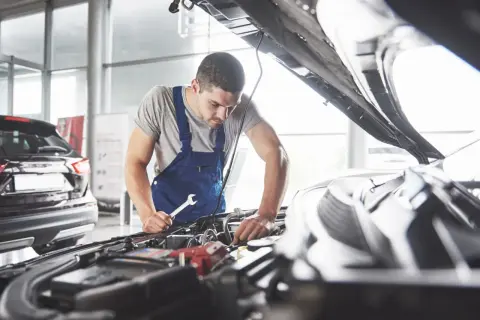 Mechanik sprawdza objawy poduszki silnika, trzymając klucz w dłoni.