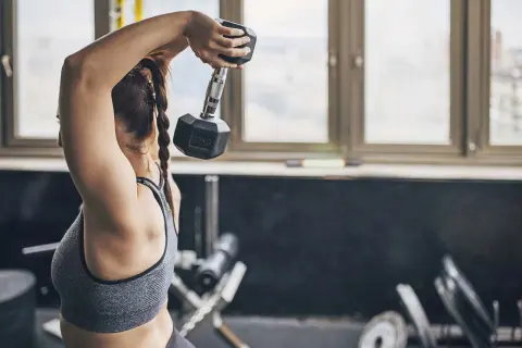 Kvinna utför tricep press med en hantel i gymmet.