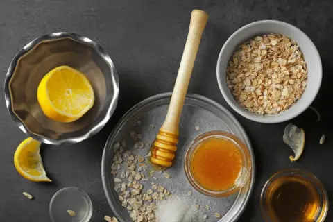 Zutaten für ein natürliches Peeling zur Hautentgiftung: Haferflocken, Honig, Zitrone und Zucker.