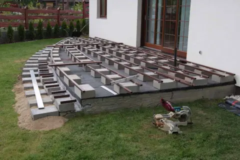 Budowa tarasu kompozytowego: betonowe bloczki podtrzymują legary, tworząc solidną podstawę.