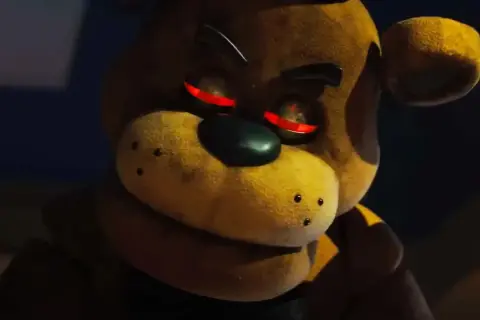 Freddy Fazbear z czerwonymi, świecącymi oczami, wygląda złowrogo w ciemności.