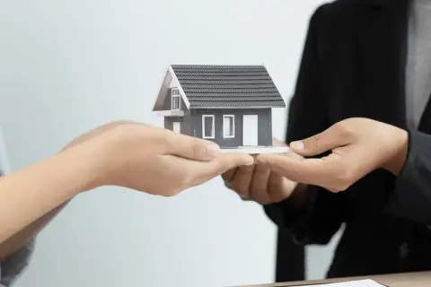 Manos intercambian una maqueta de casa, simbolizando la gestión de alquileres y la transferencia de propiedades.