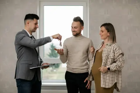Agente inmobiliario realiza la entrega de llaves de alquiler a una pareja joven, uno de ellos embarazado, en un nuevo hogar.