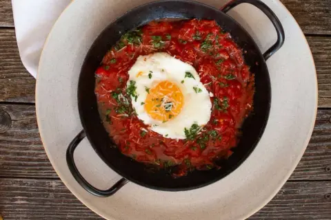 Ein Spiegelei ruht auf einer herzhaften, italienischen Tomatensauce, garniert mit Petersilie und Parmesan.