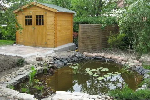 Un bassin d'agrément avec des nénuphars, une cabane en bois et une clôture en bois créent un espace paisible, préservant l'intimité du voisin.