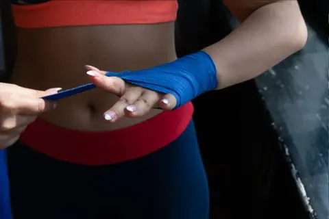 Une femme en tenue de sport prépare ses mains pour l'entraînement, montrant comment mettre des bandes de boxe bleues.