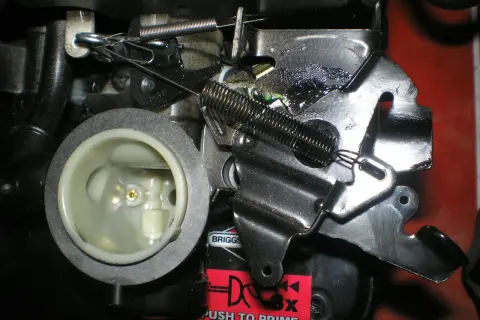 Mechanizm kosiarki z widoczną linką gazu, sprężynami i elementami gaźnika.