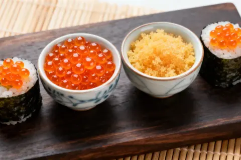 Zwei Sushi-Rollen mit Lachsrogen und eine Schale mit Masago, dem Rogen von Fischen wie Capelin.