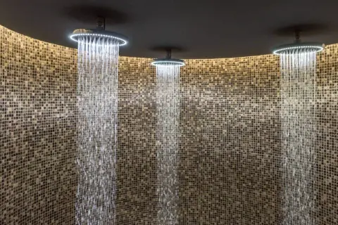 Trois douches modernes avec éclairage LED diffusent des cascades d'eau sur un mur de mosaïque. Une expérience de douche sensorielle unique.