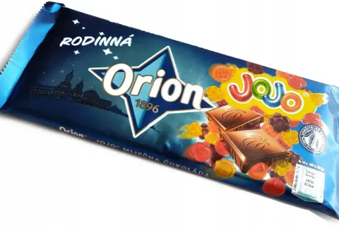 Orion Mléčná čokoláda z želkami. Kolorowe żelki w kształcie kwiatków i guzików otaczają kostki czekolady na opakowaniu.