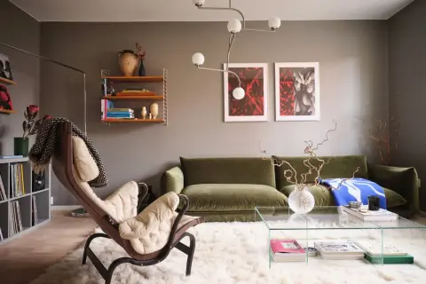 Salotto moderno con divano verde, poltrona in pelle e tessuto chiaro, tappeto bianco soffice e quadri alle pareti che creano un gioco di **colori chiari e scuri**.