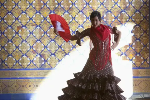 Tancerka w hiszpańskim stroju flamenco, z wachlarzem w dłoni, na tle zdobionej kafelkami ściany.