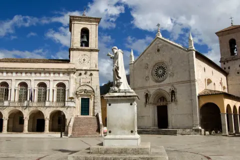 La piazza di Norcia con la basilica e il palazzo comunale, dominata dalla statua di San Benedetto. La basilica di Norcia oggi si presenta maestosa.