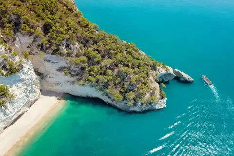 Piękna plaża i turkusowe morze, idealne miejsce, by zastanowić się, gdzie do Włoch na wakacje. Statek wycieczkowy zbliża się do skalistego wybrzeża.