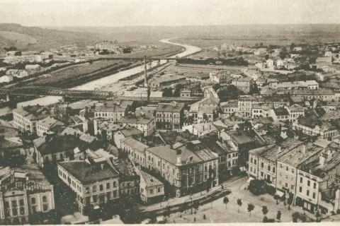 Widok z lotu ptaka na miasto z rzeką i mostami. Widać gęstą zabudowę, fabryki i wzgórza w tle. Warto przemyśl zasanie tego miejsca.