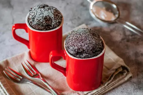 Due tortine al cioccolato in tazza, spolverate di zucchero a velo, pronte per essere gustate. Una delizia veloce da preparare al microonde.