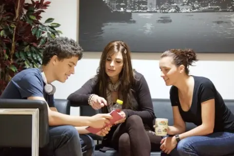 Jóvenes planeando su intercambio en Londres, sentados en un sofá, con una planta y un cuadro de la ciudad de fondo.