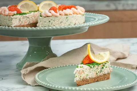 En läcker laxtårta på kavring, dekorerad med räkor, rom och citron. En bit serveras på en mintgrön tallrik.