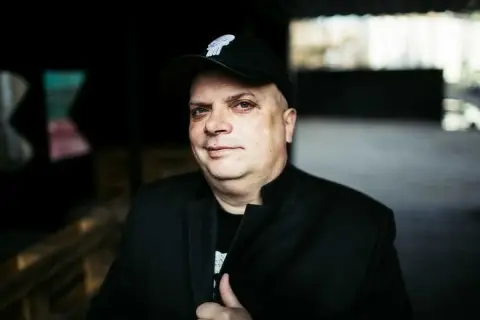 Krzysztof Skiba w czapce z daszkiem i czarnej marynarce, jakby przygotowywał się do wykonania swoich kultowych utworów.