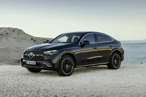 Elegancki, czarny Mercedes-Benz GLC Coupe stoi na kamienistej plaży, z widokiem na spokojne morze.