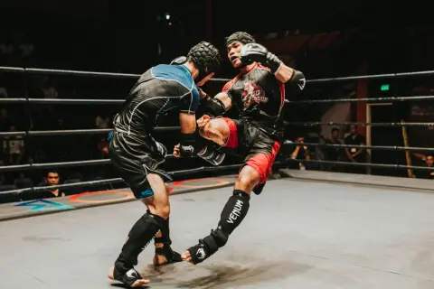 Two fighters in a ring, one delivering a powerful kick. The intensity of the moment showcases the mental fortitude and boxing psychology required for combat sports.
